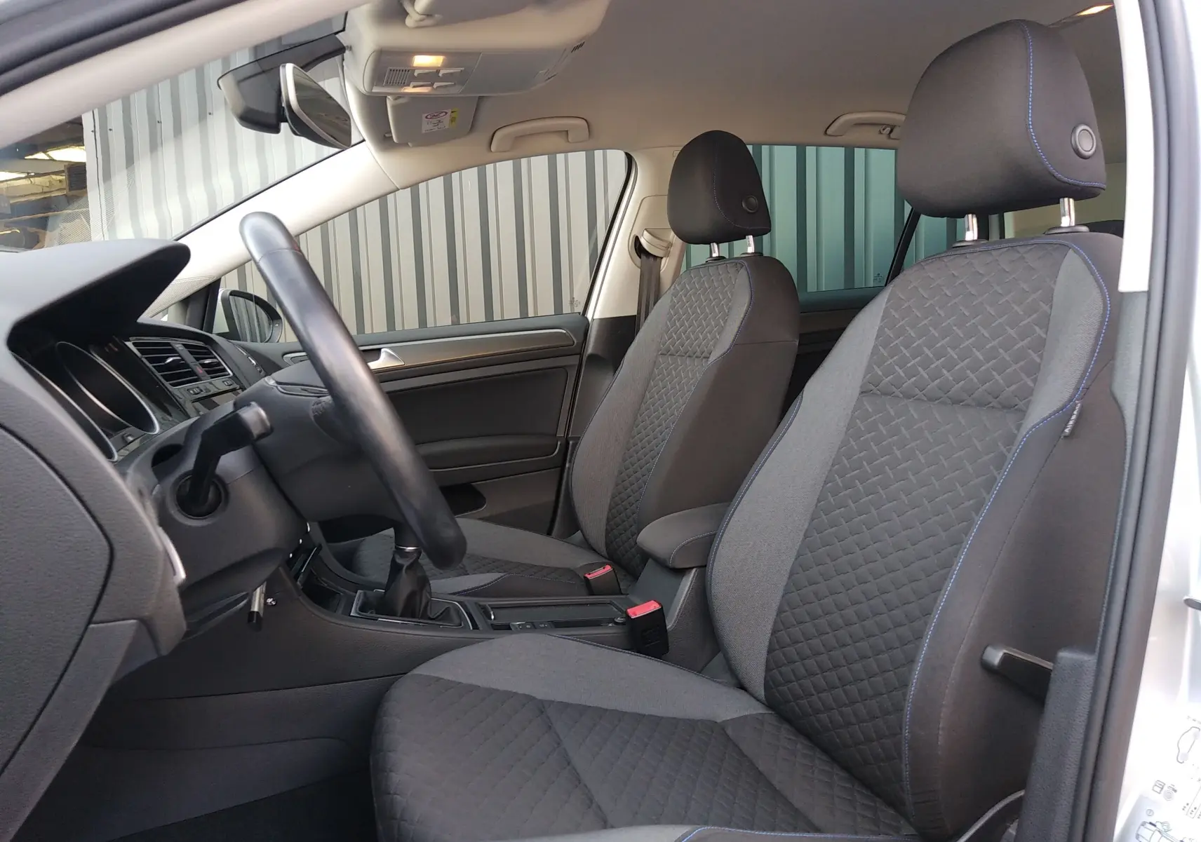 Vue intérieure côté conducteur de la Volkswagen Golf 2019, sièges tissu noir avec surpiqûres bleues et volant cuir.