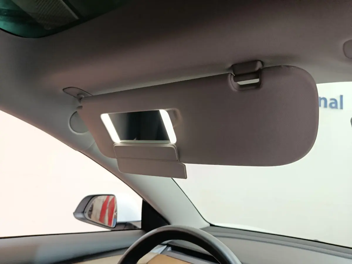 Vue intérieure côté conducteur du pare-soleil relevé avec miroir éclairé dans une Tesla Model 3 blanche 2022.