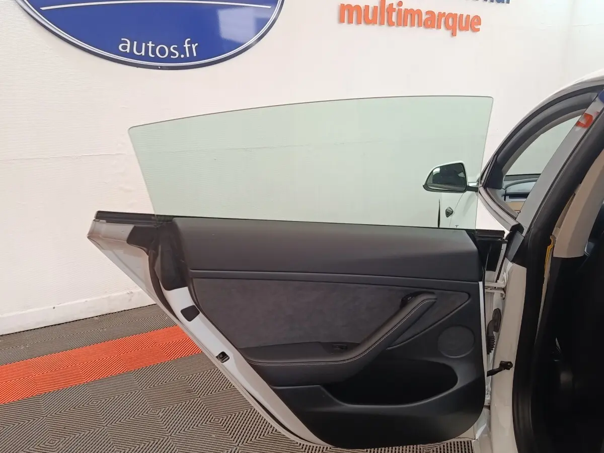 Porte arrière droite ouverte d'une Tesla Model 3 blanche, intérieur noir avec panneau de porte épuré.