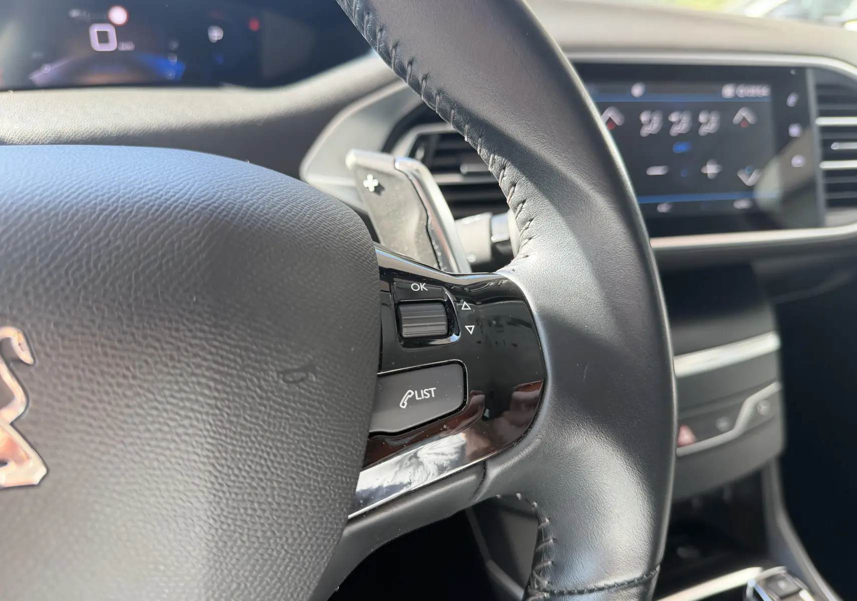 Gros plan sur le volant noir de la Peugeot 308 SW 2021 avec commandes intégrées et tableau de bord numérique flou en arrière-plan.