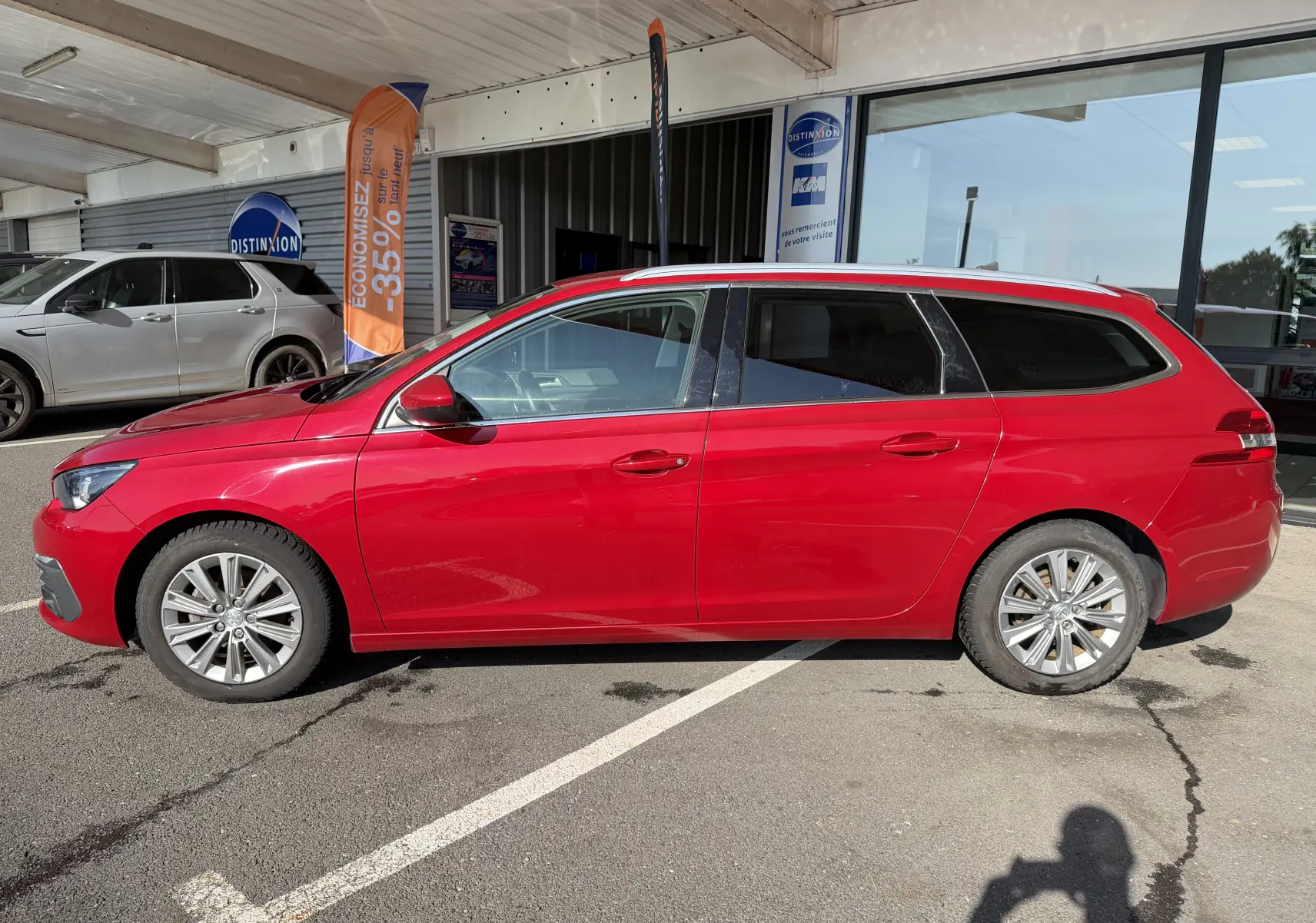 Peugeot 308 SW rouge rubis vue de profil côté gauche, break 5 portes garé devant un showroom.