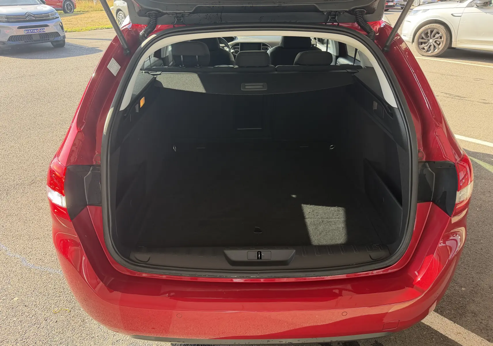 Coffre ouvert vu de l'arrière d'une Peugeot 308 SW rouge rubis, montrant l'espace de chargement vide.