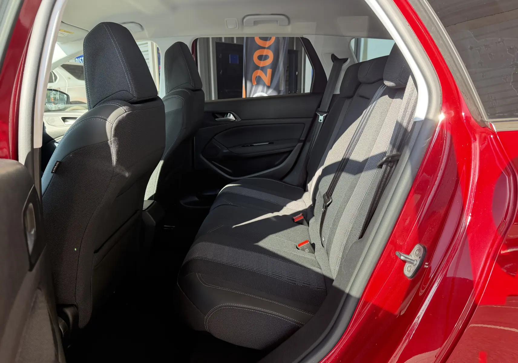 Vue intérieure côté droit sur les sièges arrière noirs d’une Peugeot 308 SW rouge rubis avec porte ouverte.