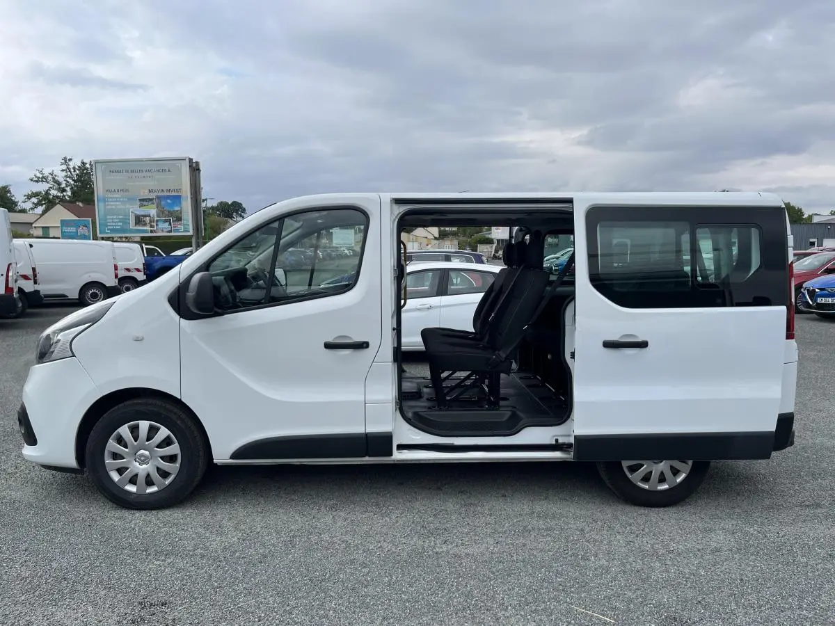Profil côté gauche d'un Renault Trafic Fourgon blanc 2016 avec porte latérale coulissante ouverte et sièges noirs visibles.