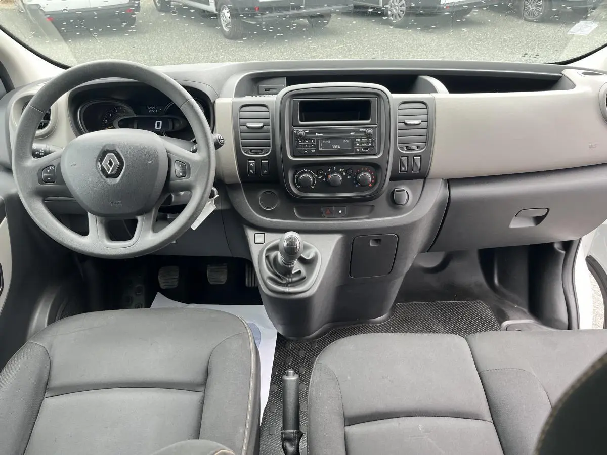 Intérieur avant du Renault Trafic Fourgon blanc 2016, tableau de bord gris clair et volant noir avec levier de vitesse manuel.