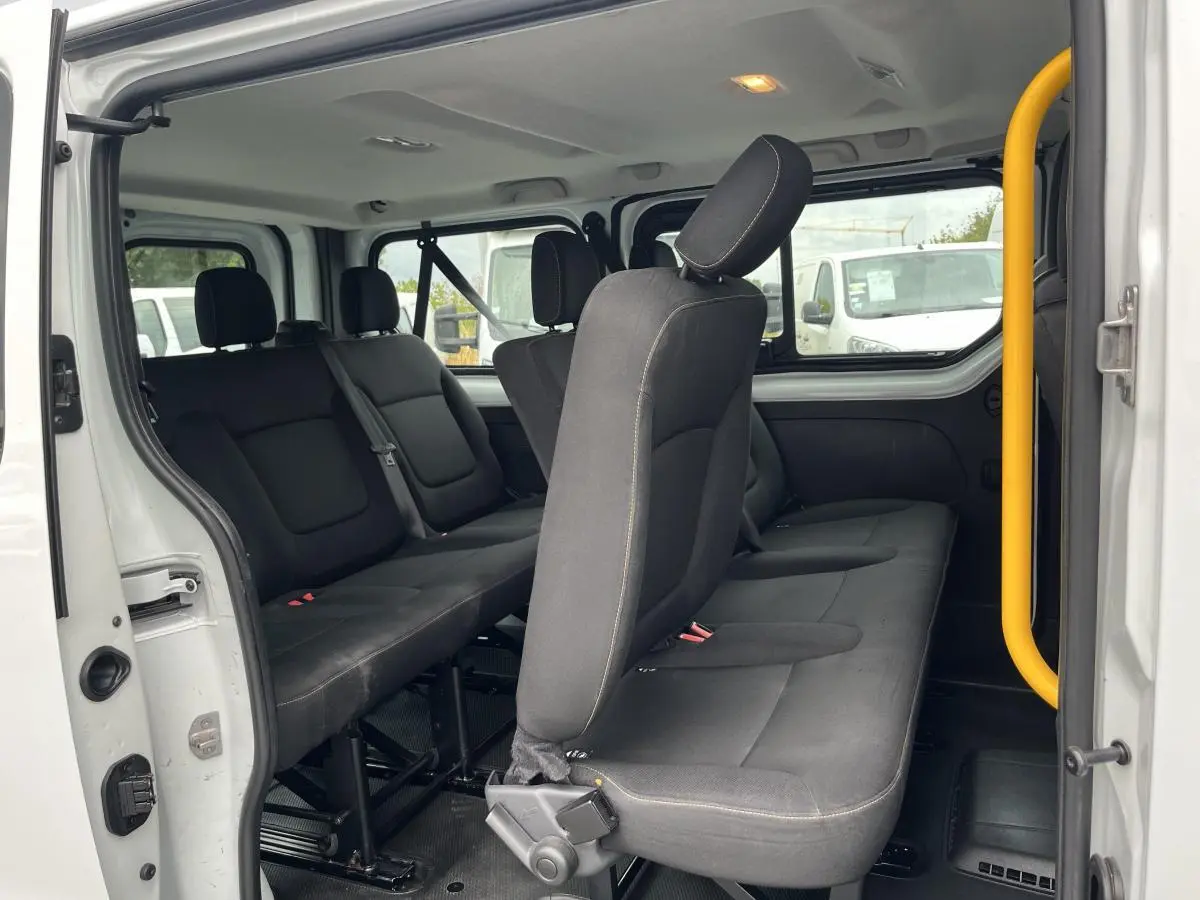 Intérieur du Renault Trafic blanc vu côté gauche, montrant les banquettes noires 3 rangées avec ceintures de sécurité.