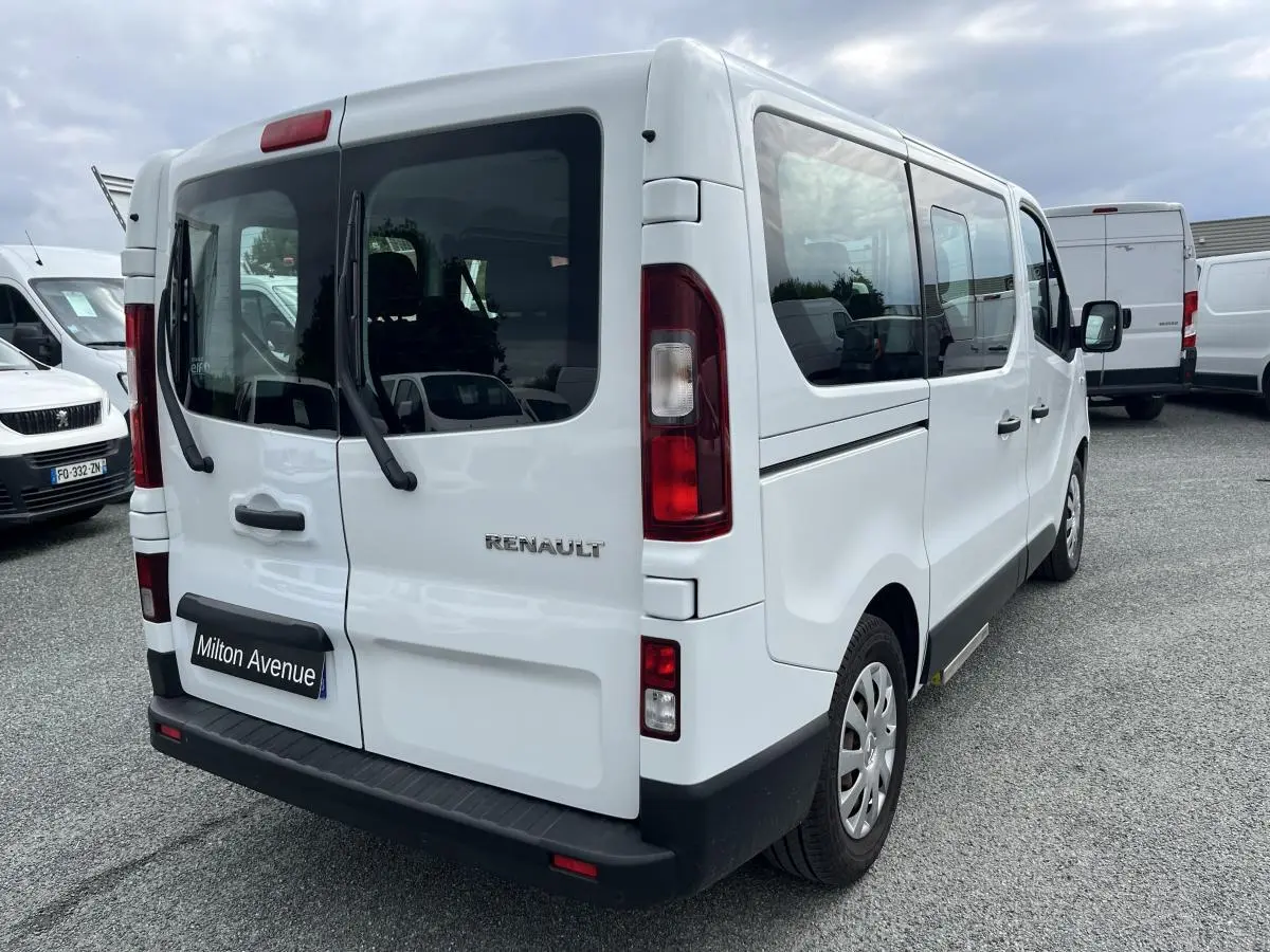 Renault Trafic Fourgon blanc vu en 3/4 arrière droit, avec portes arrière vitrées et pare-chocs noirs grainés.