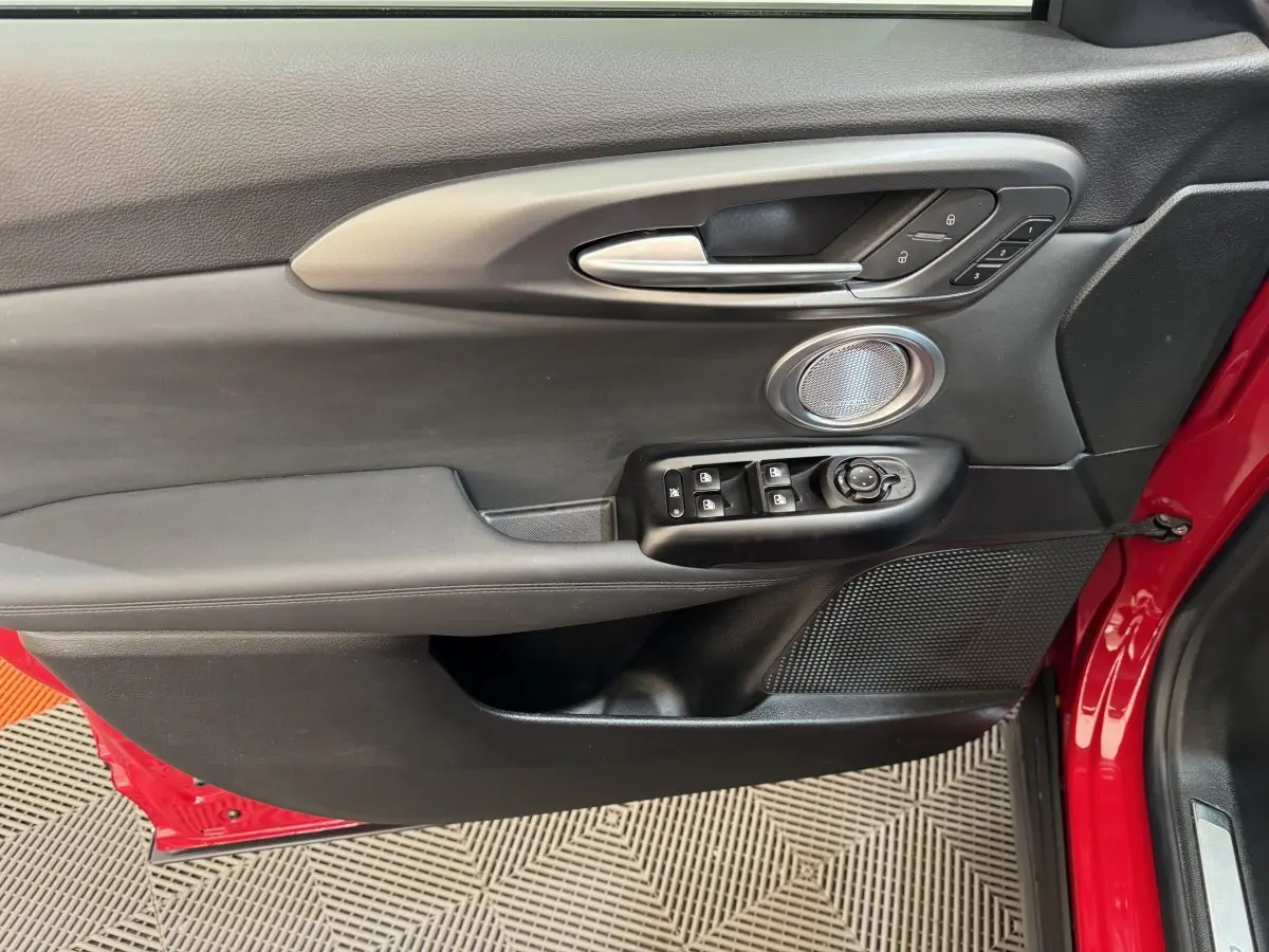 Gros plan sur la porte avant gauche rouge de l'Alfa Romeo Tonale avec commandes de vitres et haut-parleur intégré.