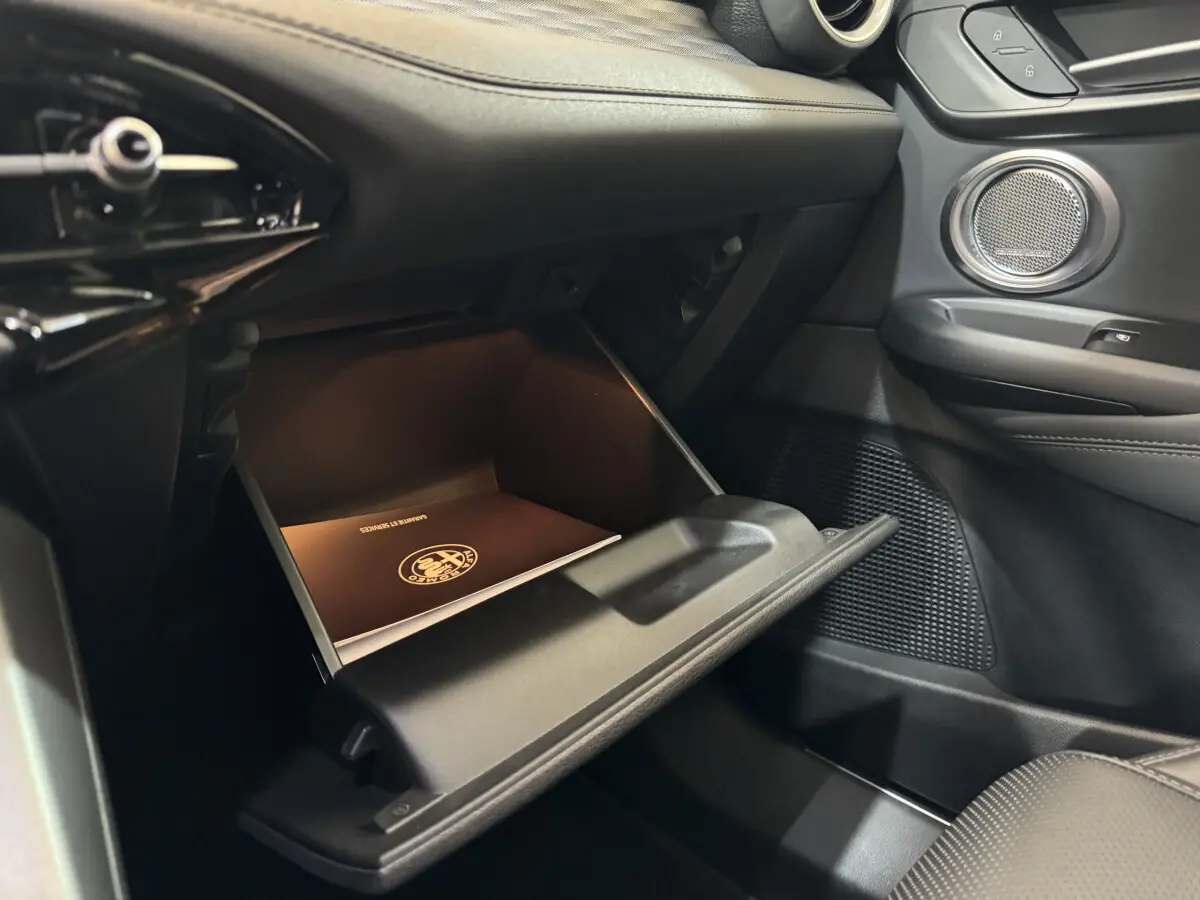 Gros plan de la boîte à gants ouverte côté passager de l'Alfa Romeo Tonale rouge avec manuel de bord visible.