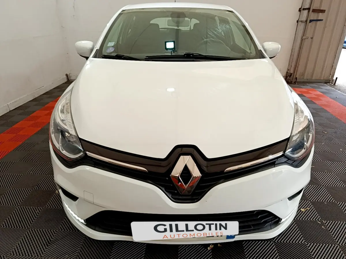 Vue frontale d'une Renault Clio Business TCe 90 blanche avec logo chromé et feux LED dans un garage.