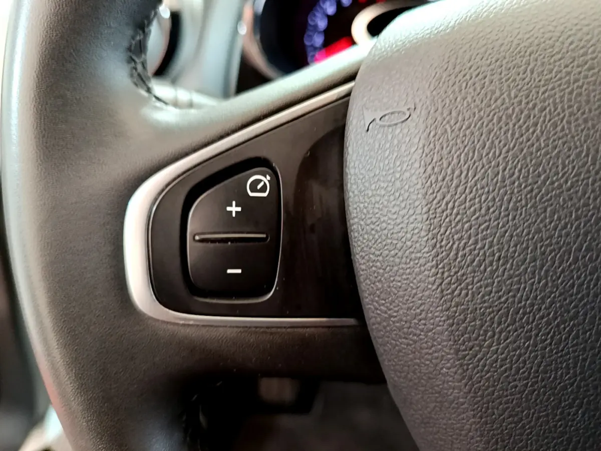 Gros plan sur les commandes du régulateur de vitesse au volant cuir noir d'une Renault Clio Business blanche de 2019.