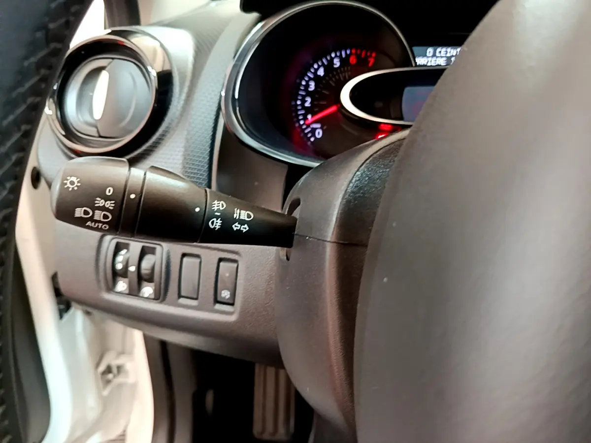 Gros plan sur la commande des phares et clignotants côté gauche du volant cuir d'une Renault Clio Business blanche de 2019.