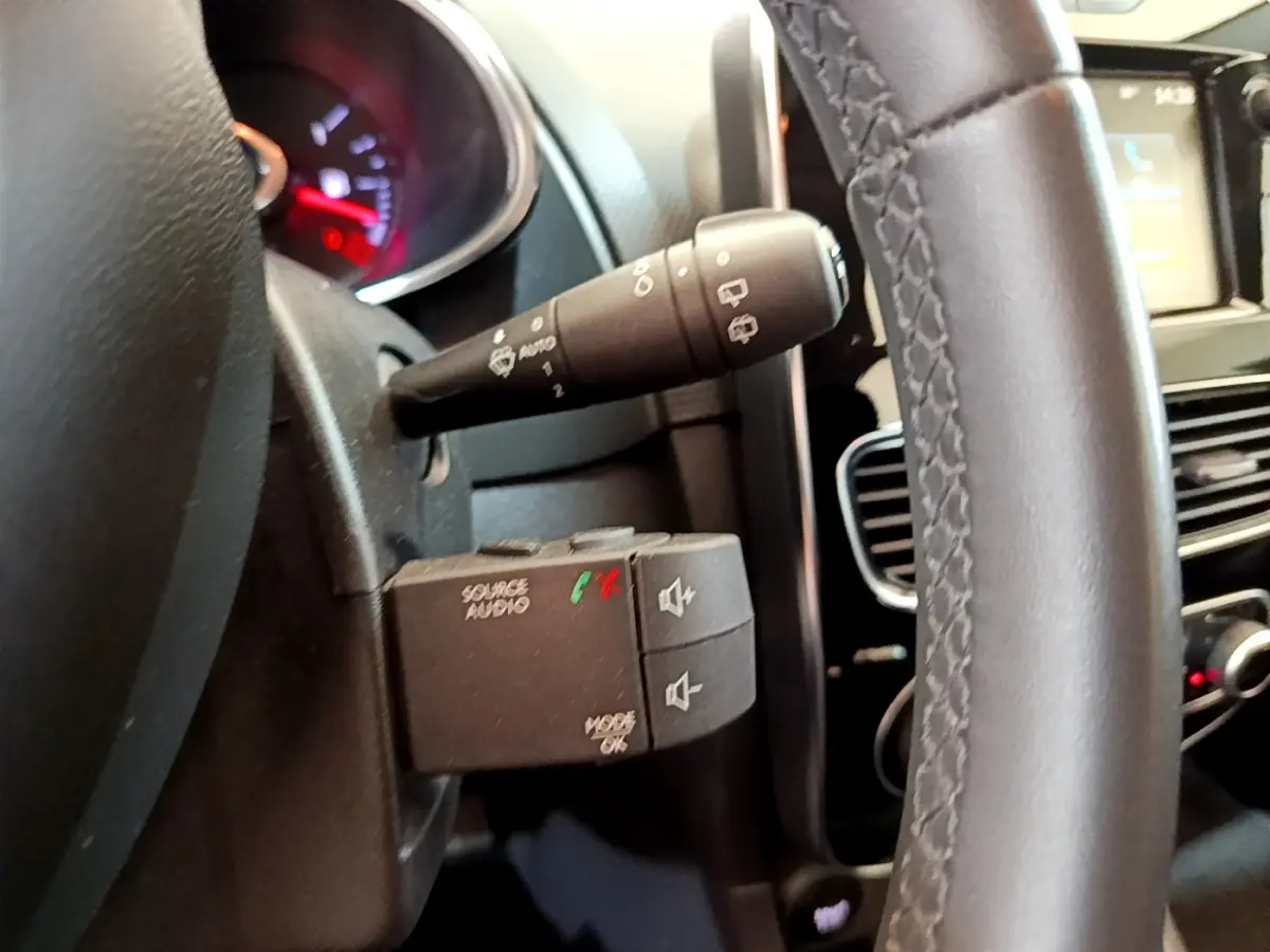 Gros plan sur la commande audio au volant cuir noir d'une Renault Clio Business TCe 90 blanche, tableau de bord en arrière-plan.