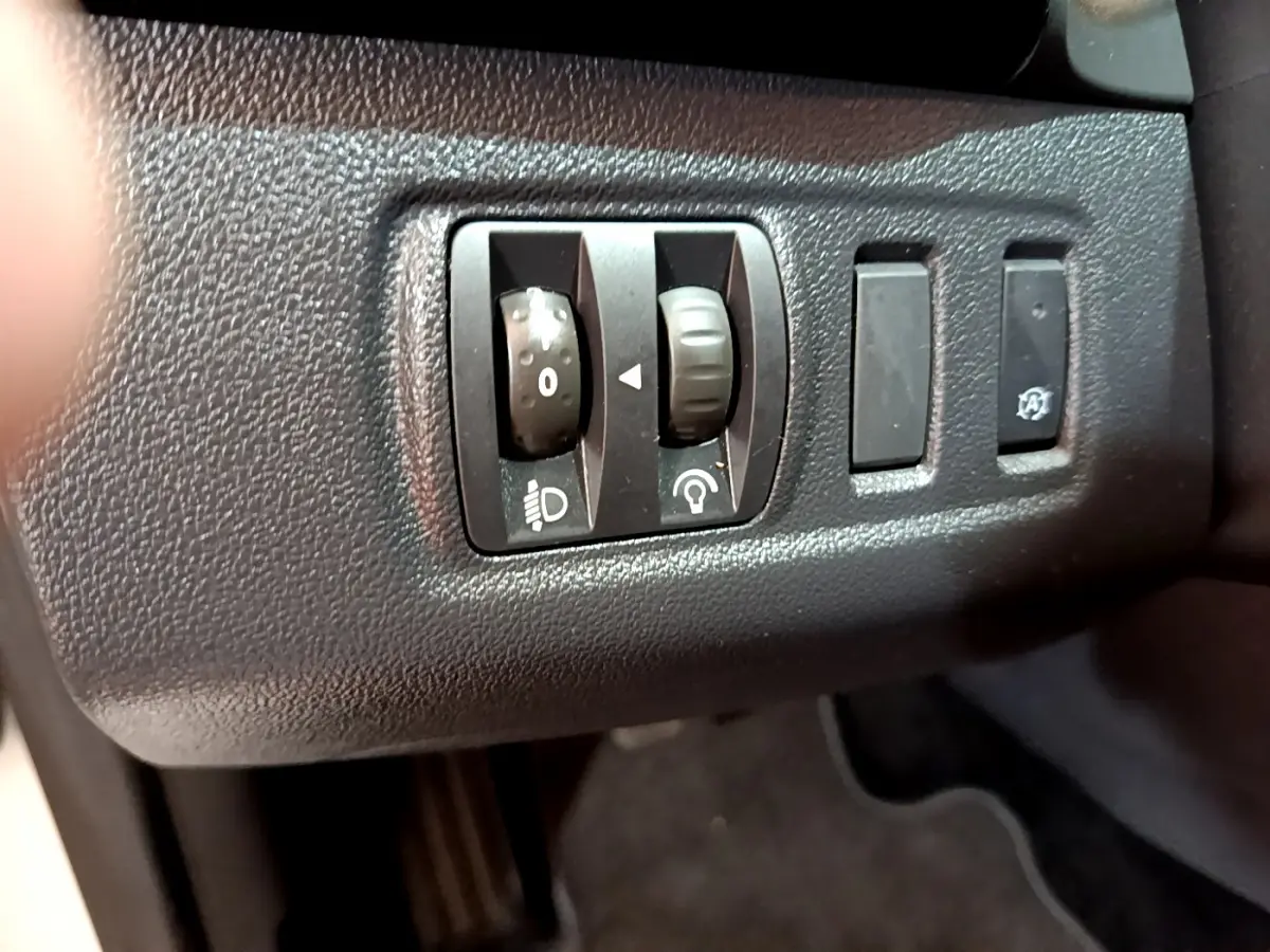 Gros plan sur les commandes de réglage des phares et tableau de bord noir dans une Renault Clio Business blanche de 2019.