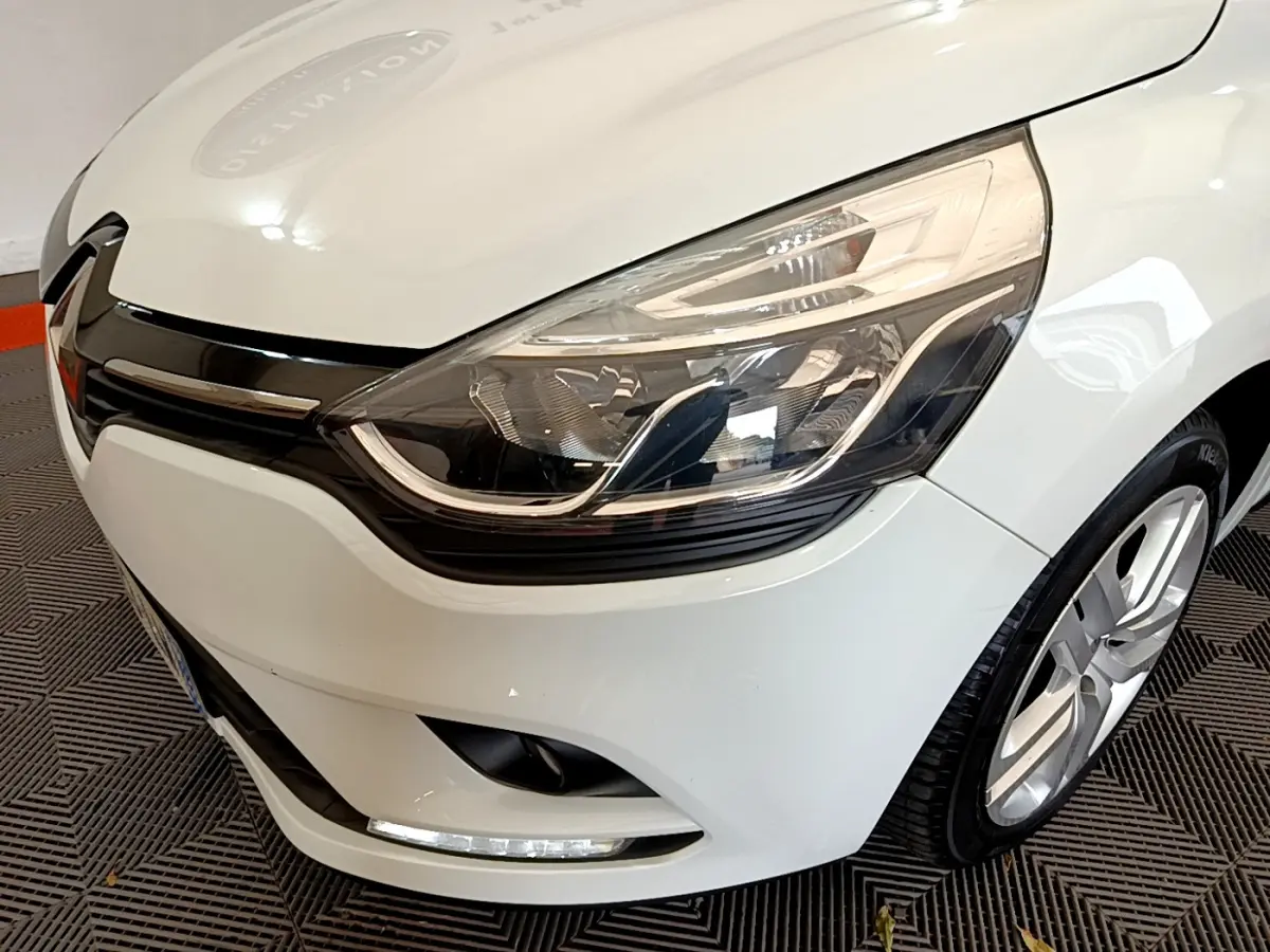 Gros plan sur l'avant droit d'une Renault Clio Business TCe 90 blanche, mettant en valeur son phare LED et la calandre noire.
