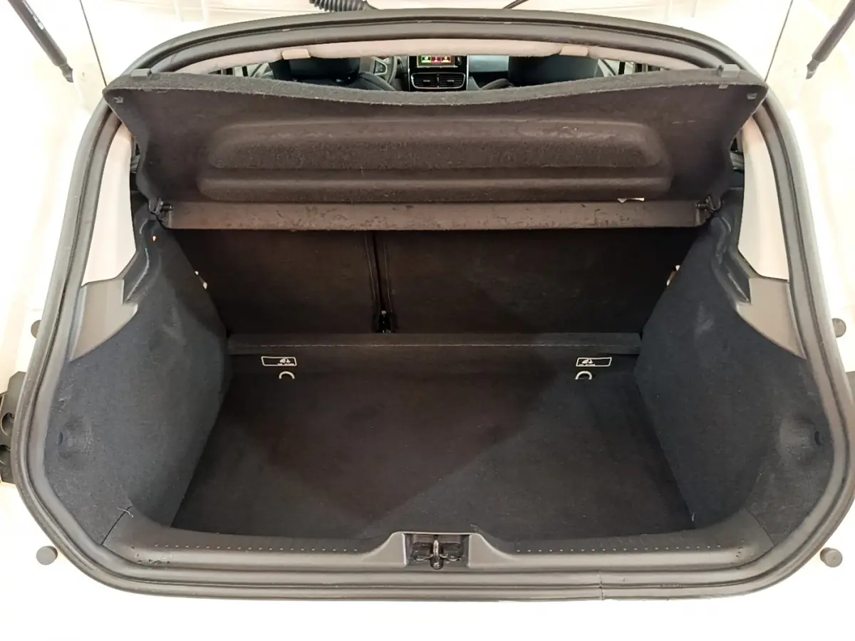 Coffre ouvert vu de l'arrière d'une Renault Clio Business blanche, intérieur noir et tablette de coffre relevée.