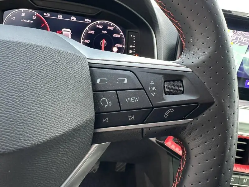 Gros plan sur la partie droite du volant perforé avec surpiqûres rouges d'une SEAT Ibiza 2025, tableau de bord numérique visible.