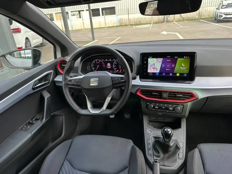 Vue intérieure avant de la SEAT Ibiza 1.0 TSI FR 2025, tableau de bord avec écran tactile et détails rouges autour des aérateurs.