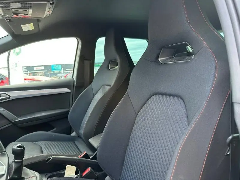 Vue intérieure côté gauche de la SEAT Ibiza 1.0 TSI FR 2025, sièges sport noirs avec surpiqûres rouges et levier de vitesses manuel.