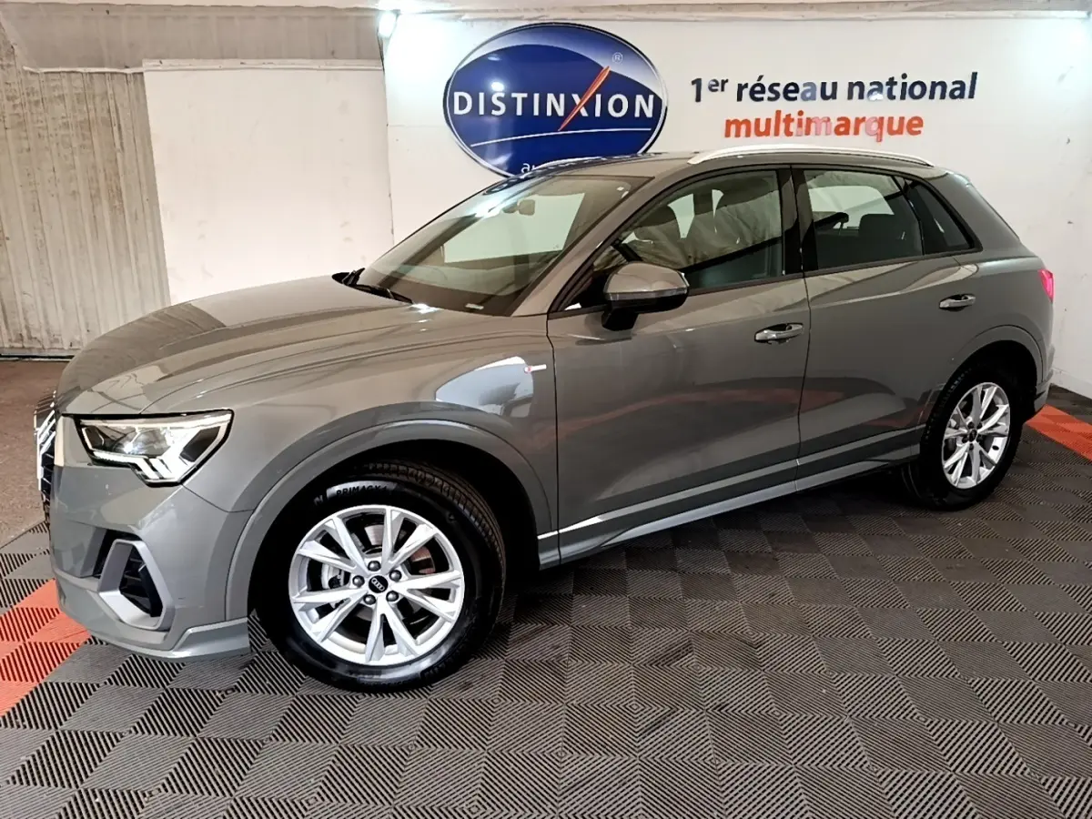 Audi Q3 gris foncé vue 3/4 avant droit, avec jantes alliage et rétroviseurs assortis dans un showroom.