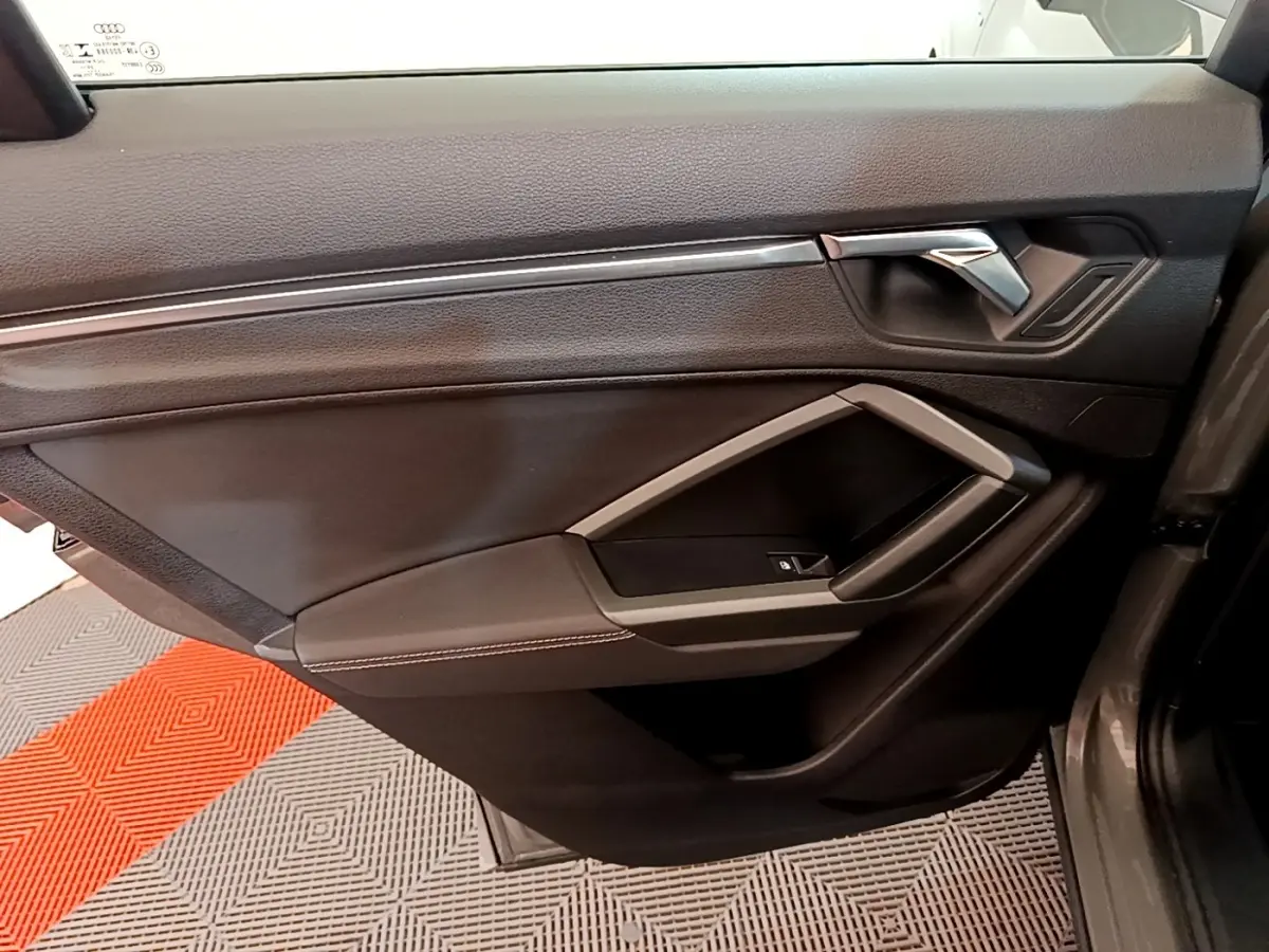 Vue intérieure du panneau de porte avant droit de l'Audi Q3 gris foncé, avec poignée chromée et accoudoir noir.