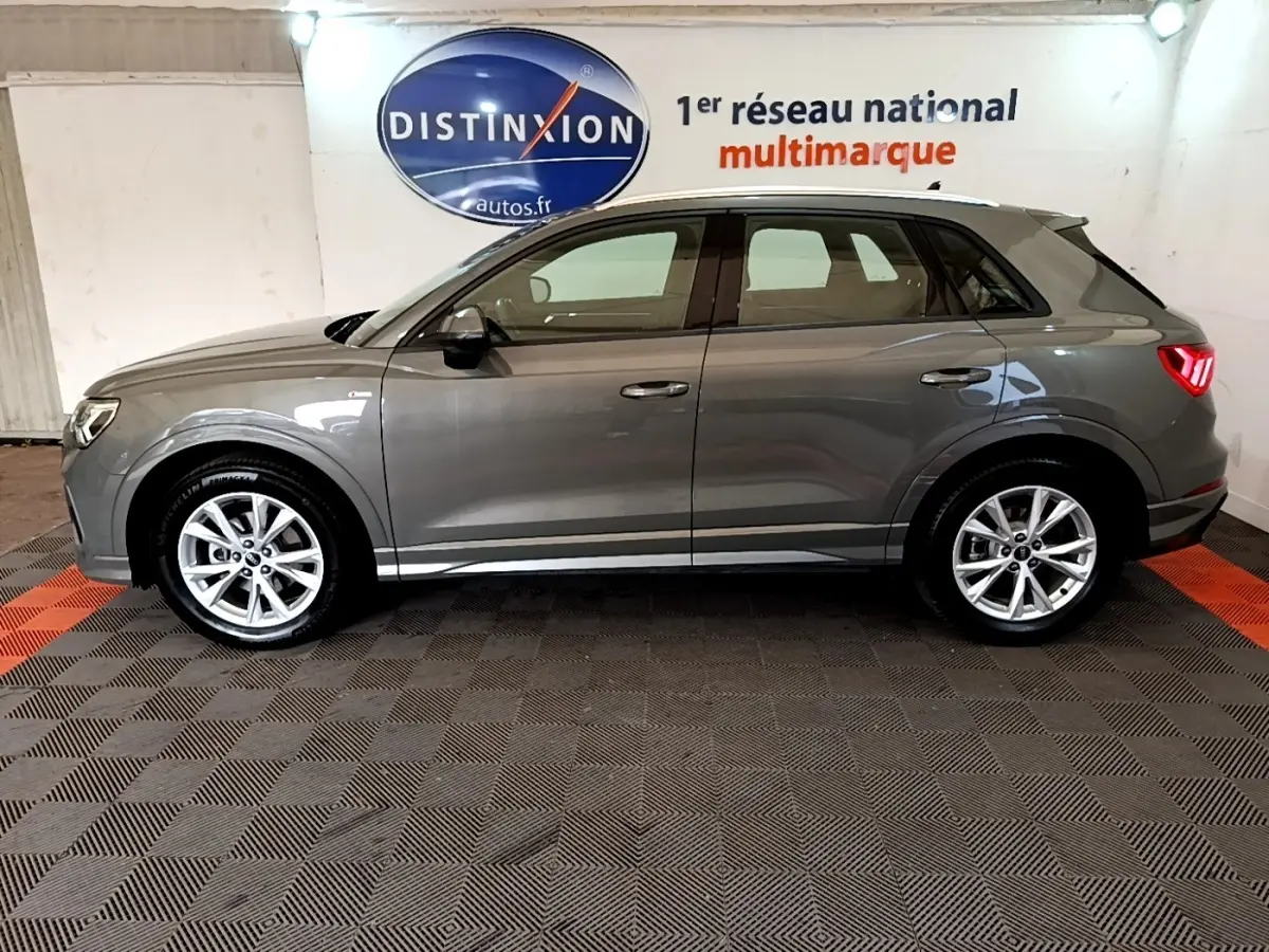 Vue de profil côté gauche d'un Audi Q3 35 TFSI gris foncé avec jantes alliage et feux arrière LED allumés.