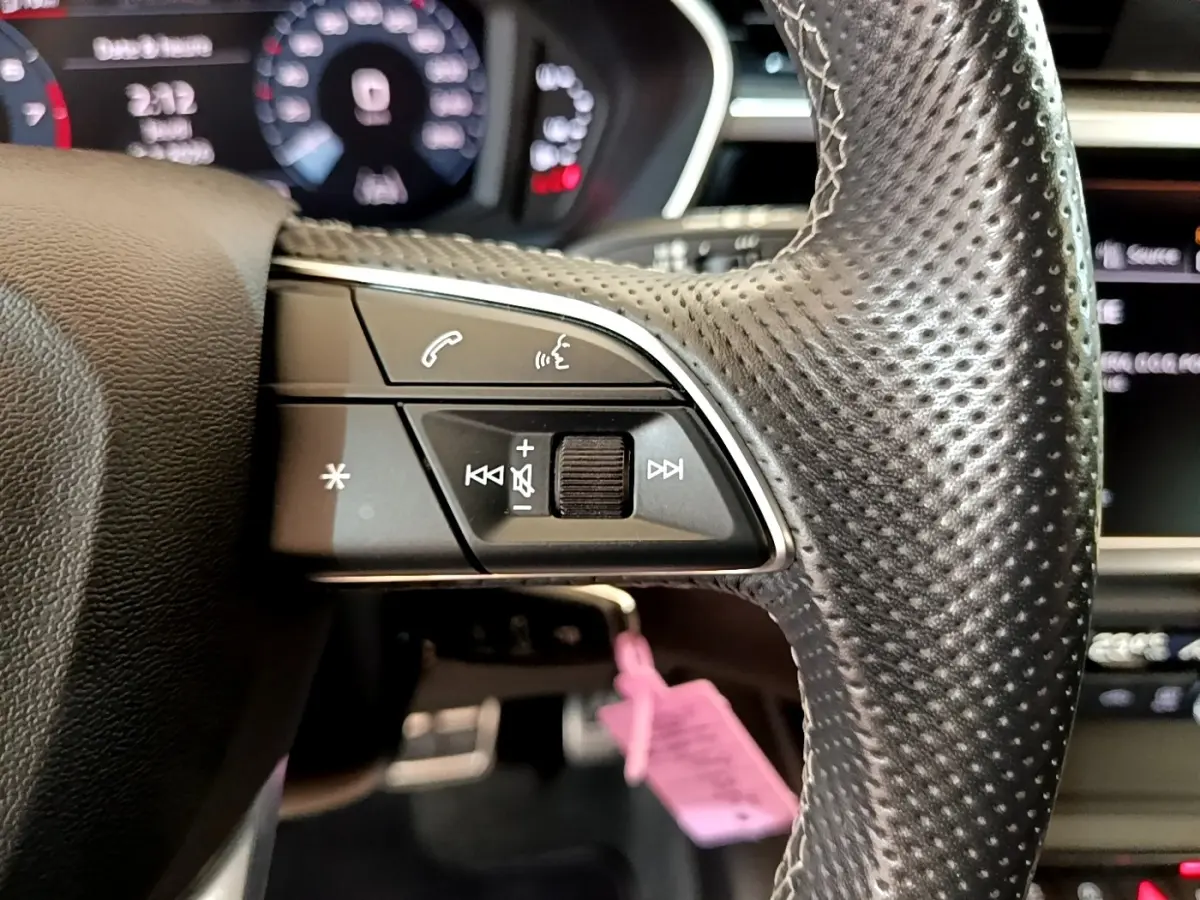 Gros plan sur le côté gauche du volant cuir perforé de l'Audi Q3 gris foncé avec commandes audio et téléphone intégrées.