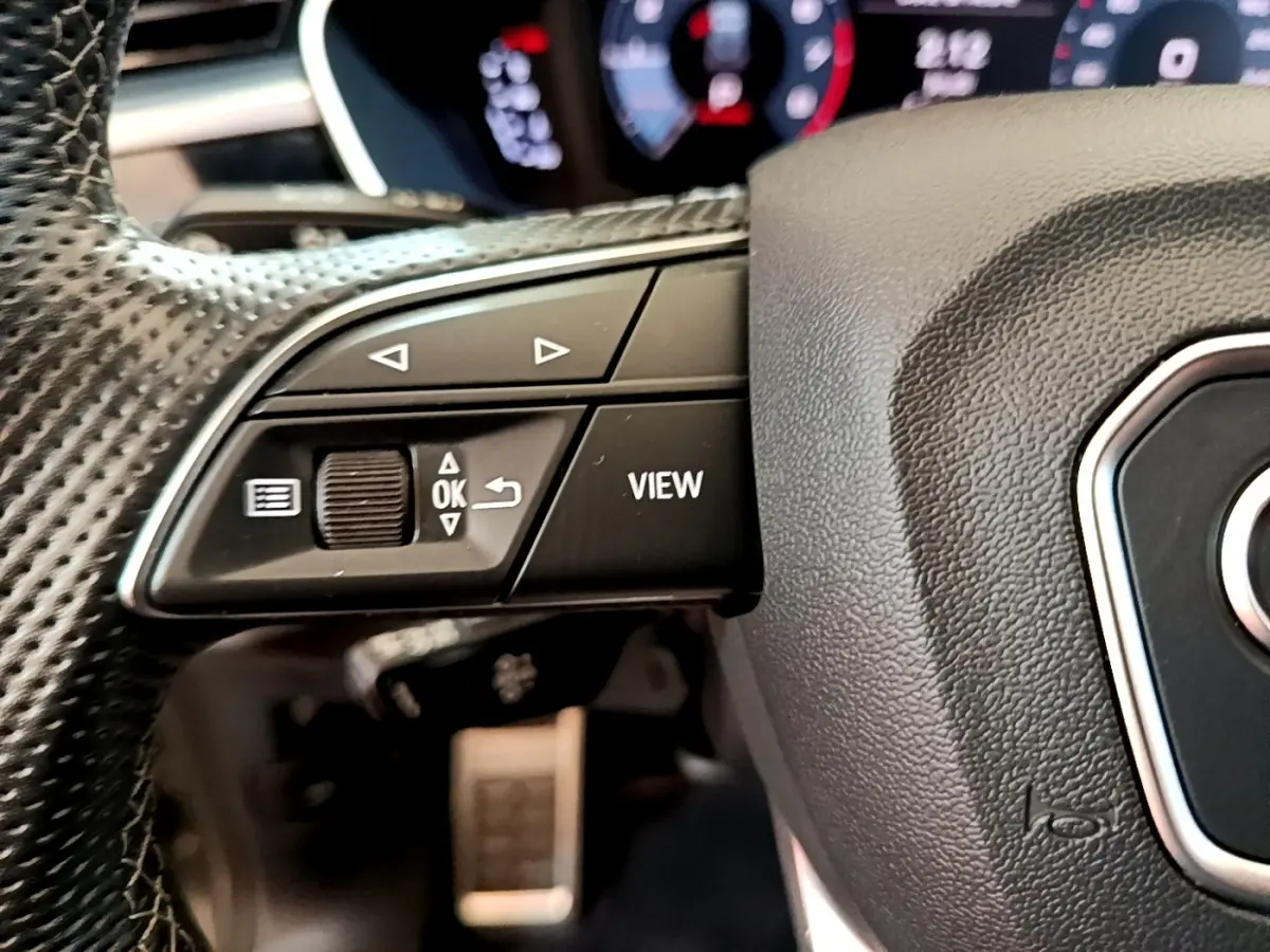 Gros plan sur le volant cuir multifonctions de l'Audi Q3 35 TFSI S Line, boutons de commande et affichage partiel en arrière-plan.