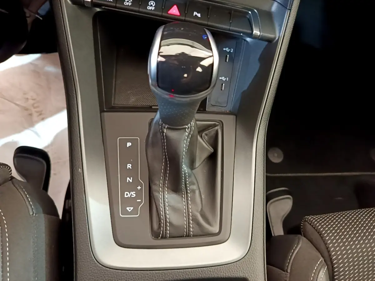 Gros plan sur la commande de la boîte automatique cuir noir avec surpiqûres blanches dans l’Audi Q3 gris foncé.