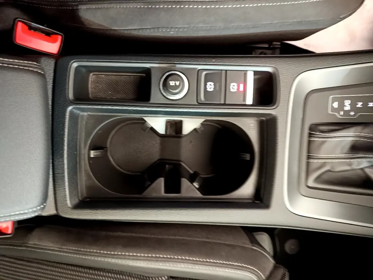 Vue plongeante sur la console centrale noire de l’Audi Q3 35 TFSI 150 MHEV S Line avec porte-gobelets et commandes frein à main électrique.