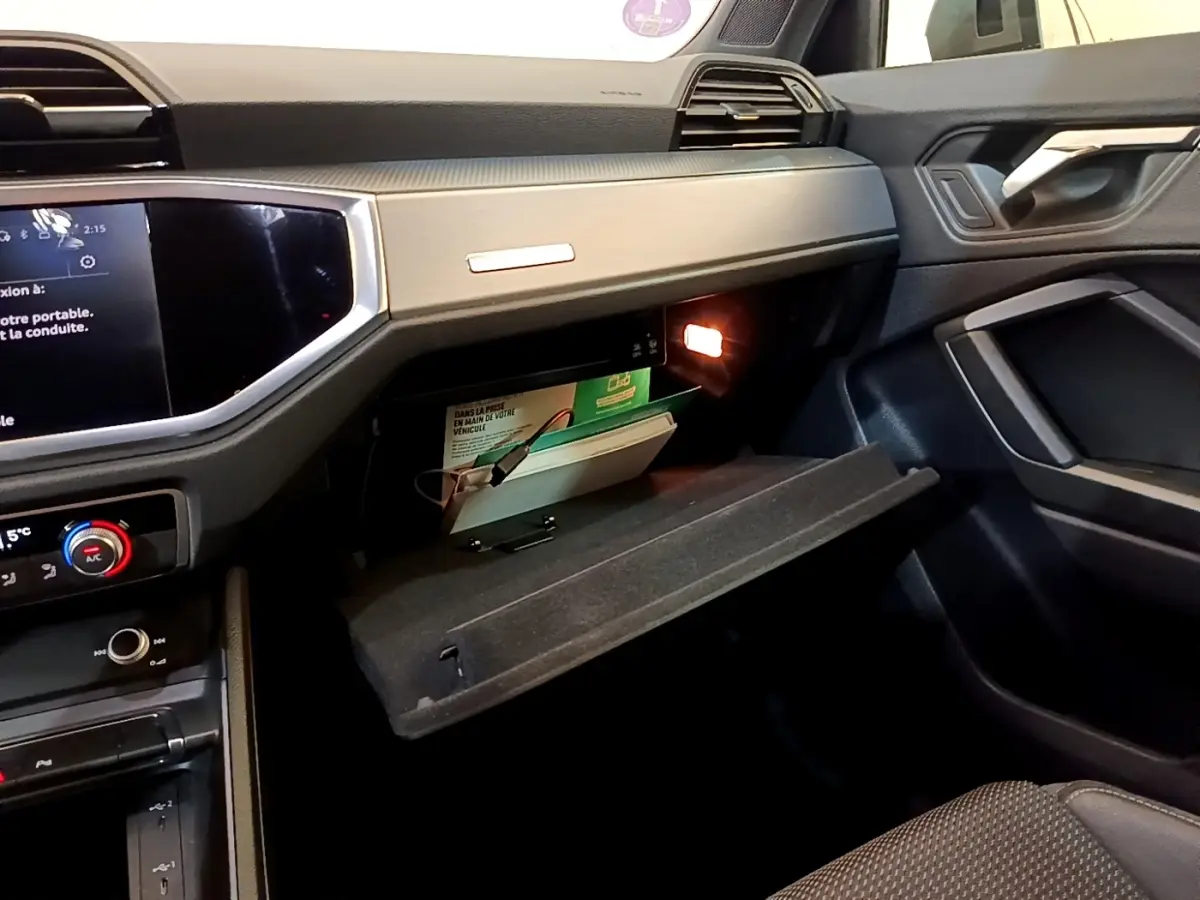 Vue intérieure côté passager de l'Audi Q3 35 TFSI 2021 avec boîte à gants ouverte et éclairage intérieur allumé.