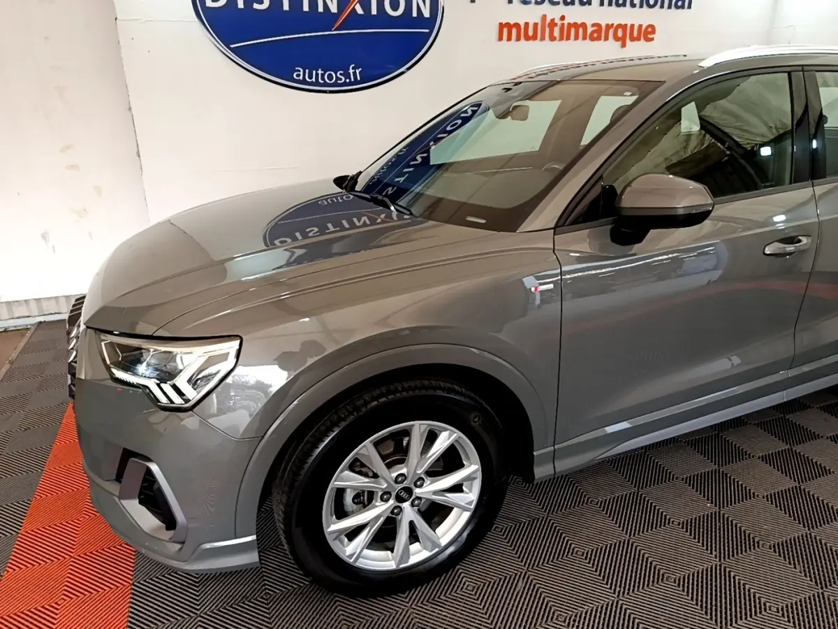 Vue 3/4 avant gauche d'un Audi Q3 gris foncé avec jantes alliage et logo S line sur l'aile avant.