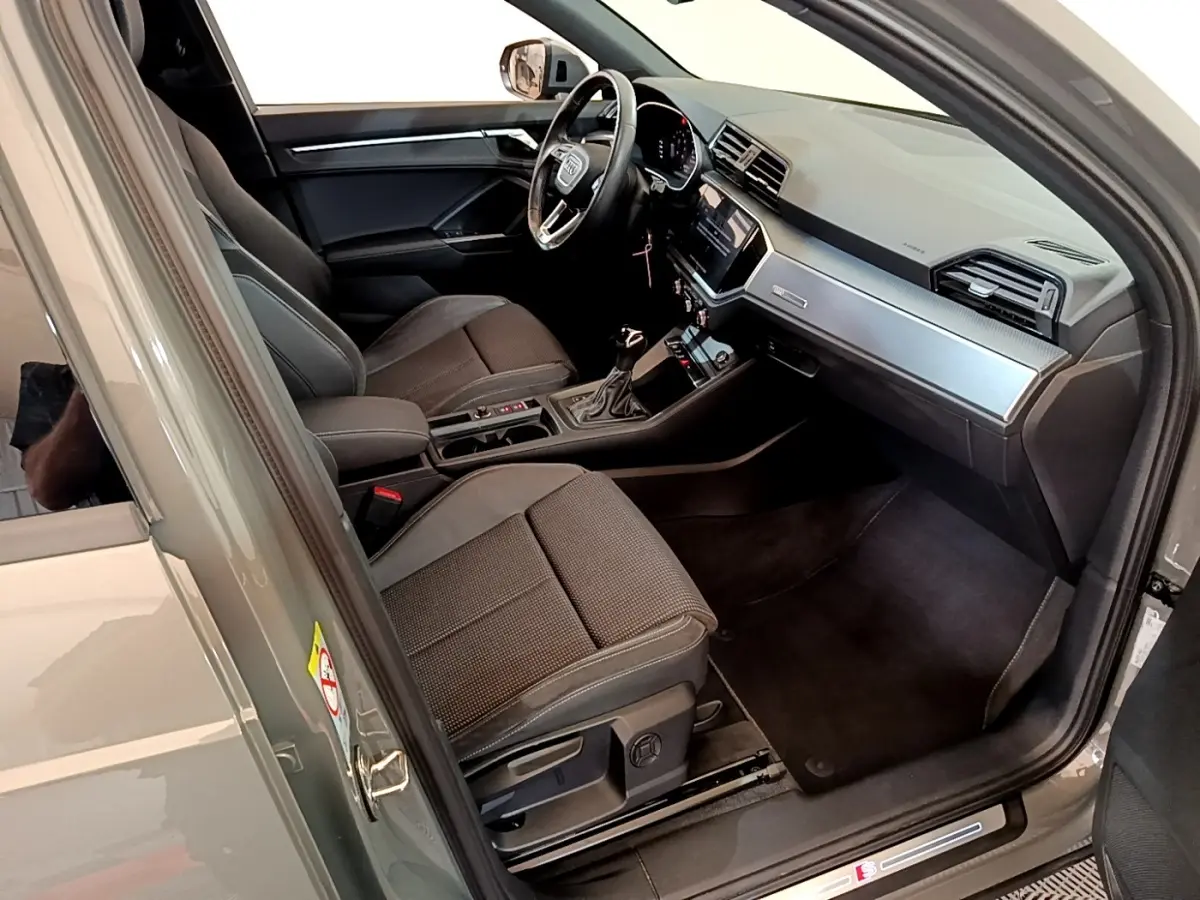 Vue intérieure côté conducteur de l'Audi Q3 gris foncé, mettant en valeur le volant cuir multifonctions et le tableau de bord moderne.