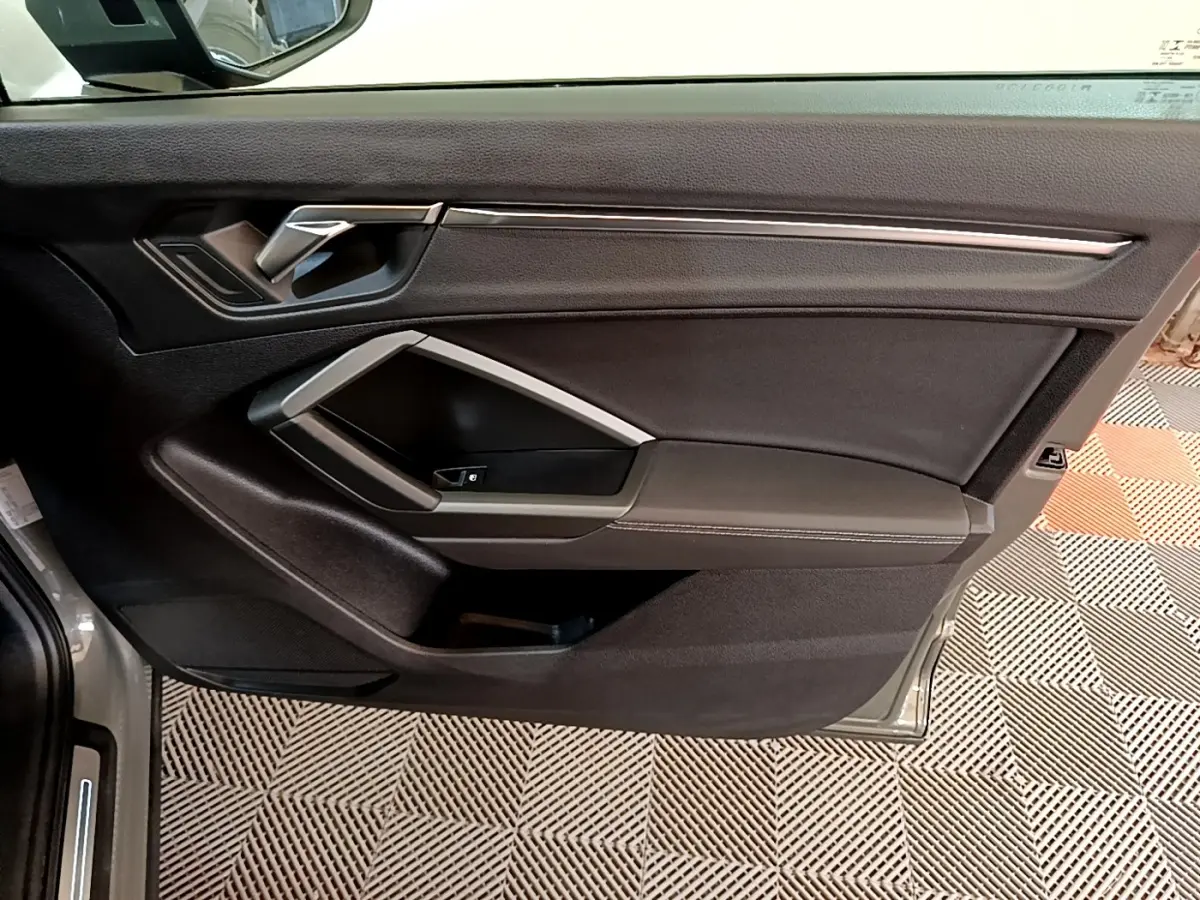 Vue intérieure de la porte avant gauche de l'Audi Q3 gris foncé, avec poignée argentée et garniture noire.