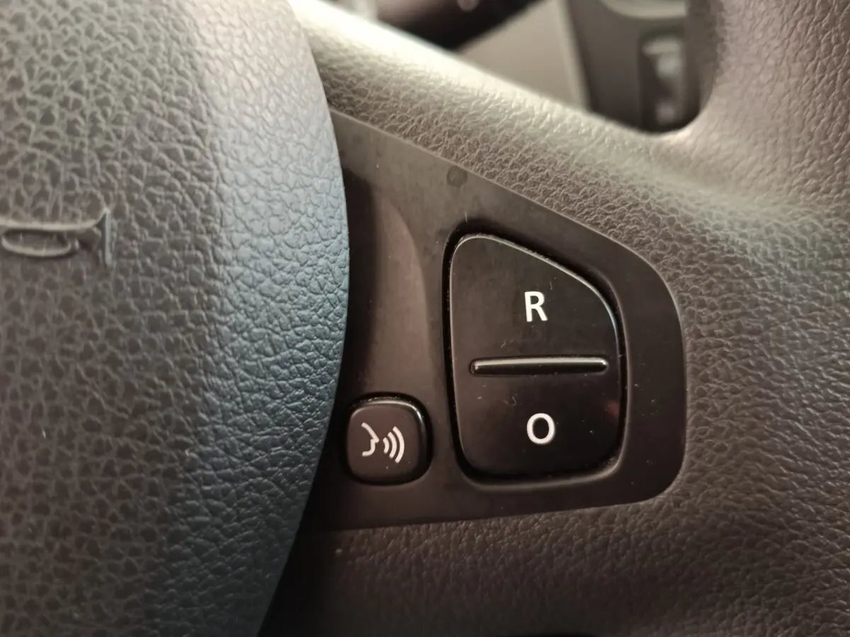 Gros plan sur les boutons de commande du volant noir du Renault Trafic Fourgon blanc, côté gauche.