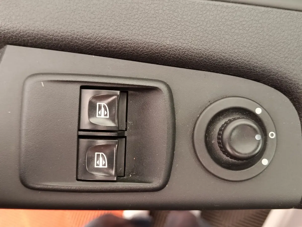 Gros plan sur les commandes électriques des vitres et le réglage des rétroviseurs d’un Renault Trafic Fourgon blanc de 2017.