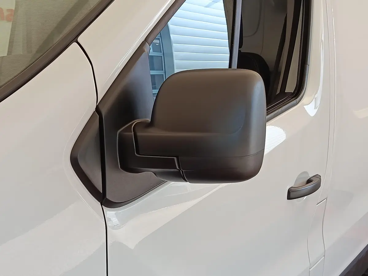 Rétroviseur noir en gros plan sur la porte côté conducteur d’un Renault Trafic fourgon blanc, vue latérale.