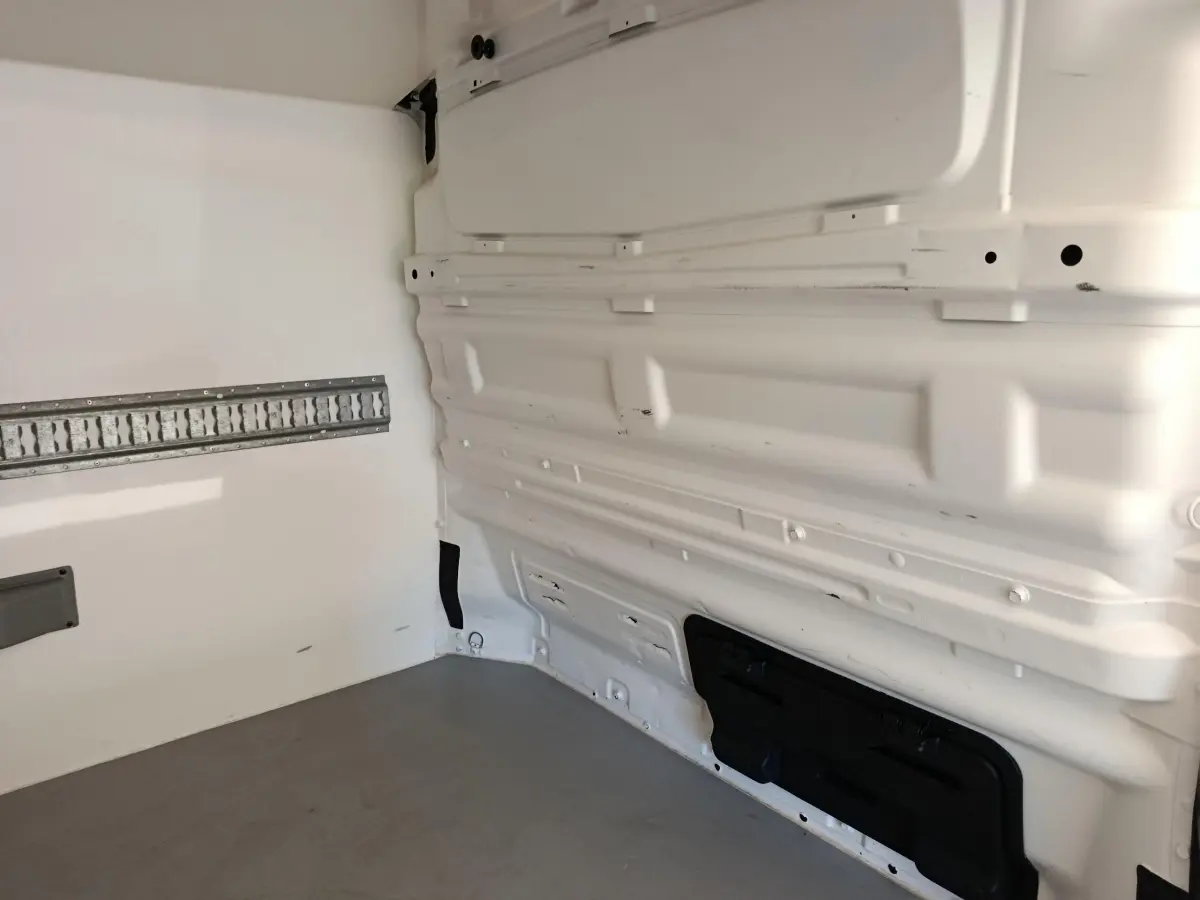 Intérieur du fourgon Renault Trafic blanc, vue latérale droite montrant la cloison pleine et le plancher gris.