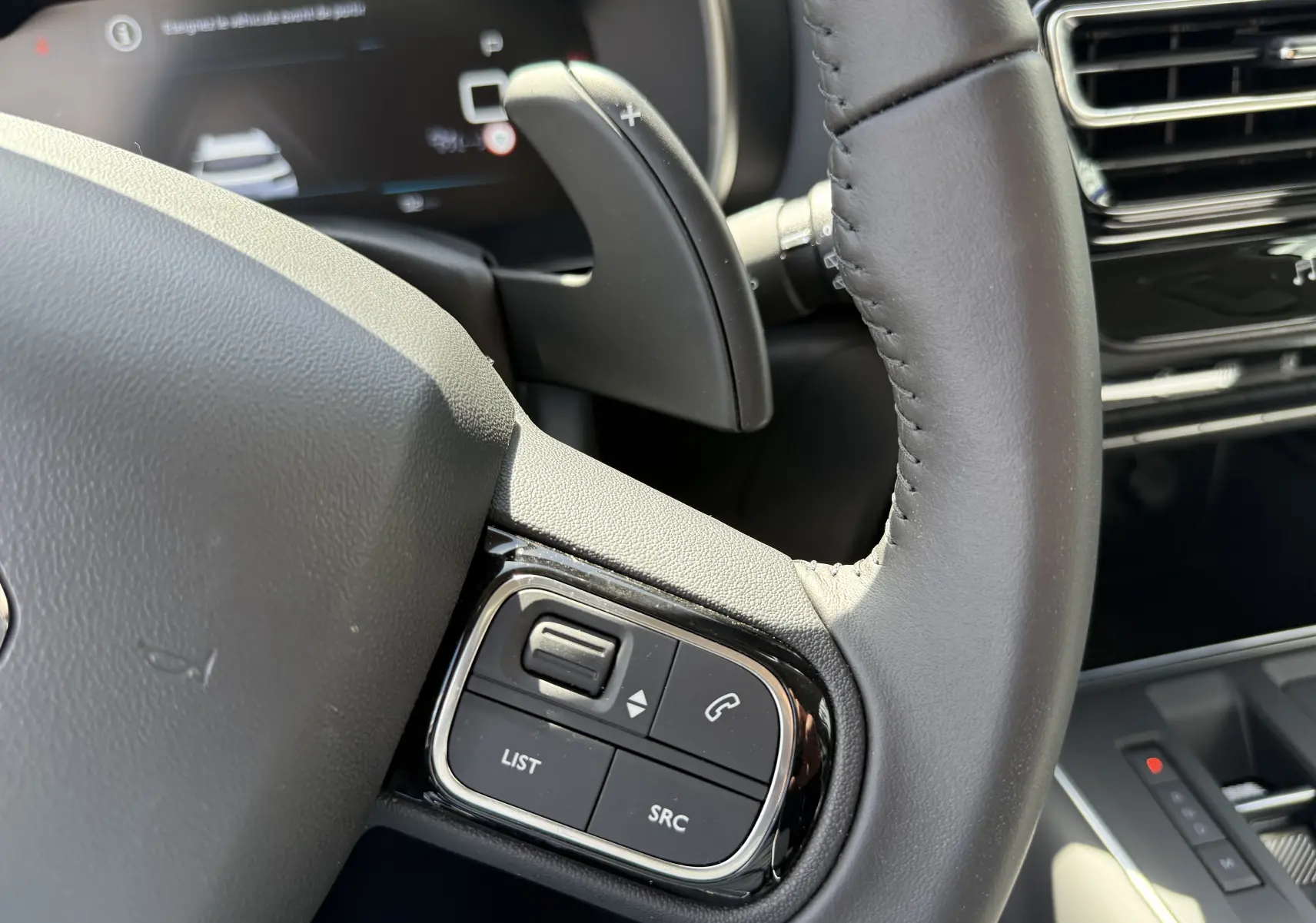 Gros plan sur le volant en cuir noir du Citroën C5 Aircross Hybrid 2025, avec commandes intégrées et palettes de changement de vitesse.