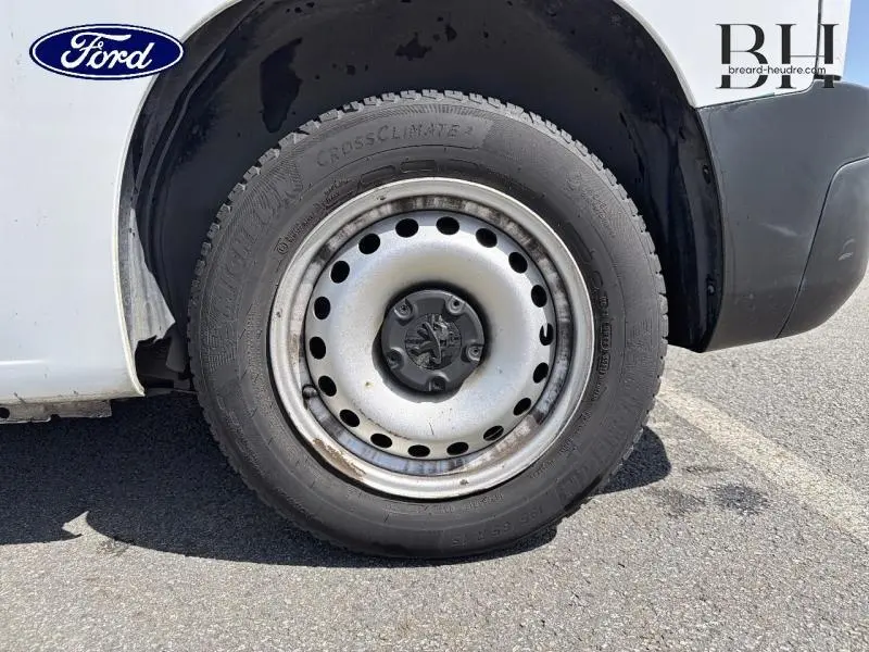 Gros plan sur la roue avant droite d’un Peugeot Partner blanc avec jante acier et logo Peugeot au centre.