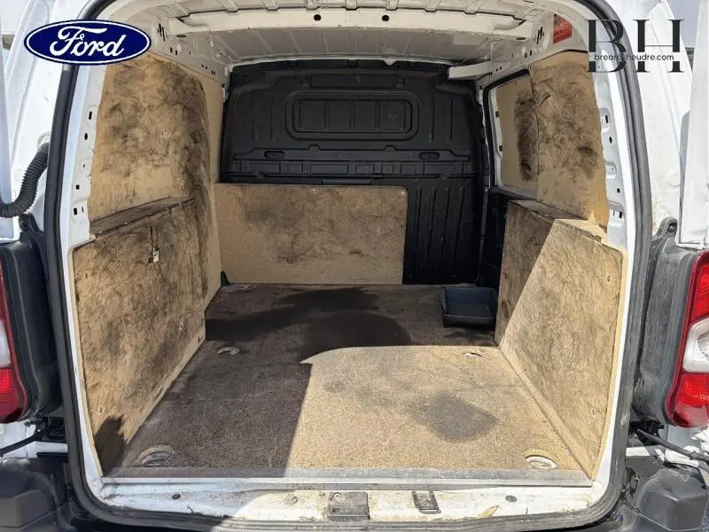 Vue arrière intérieure du Peugeot Partner blanc, montrant l'espace de chargement avec revêtement usé et cloison noire.