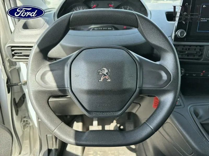 Vue rapprochée du volant noir du Peugeot Partner blanc, mettant en valeur le logo lion au centre et le tableau de bord.