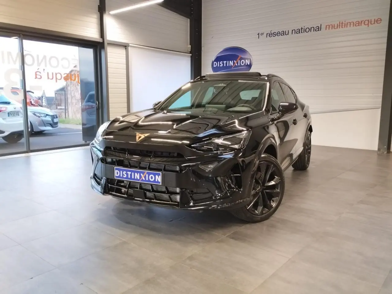 Vue 3/4 avant d'un CUPRA Formentor noir métal avec jantes noires, dans un showroom lumineux.