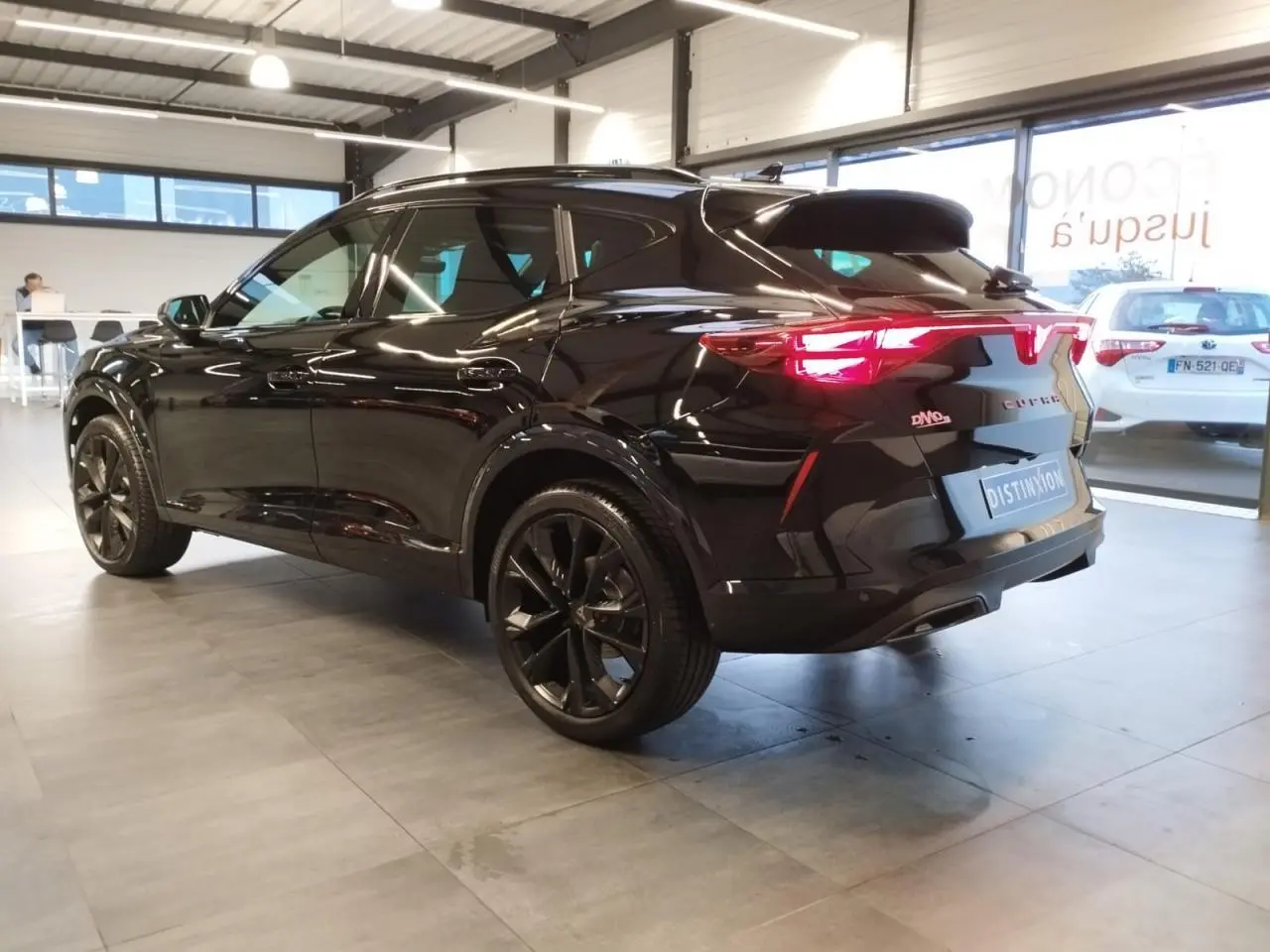 Vue 3/4 arrière droite du CUPRA Formentor noir métal avec jantes noires et feux arrière Tri-LED allumés en showroom.