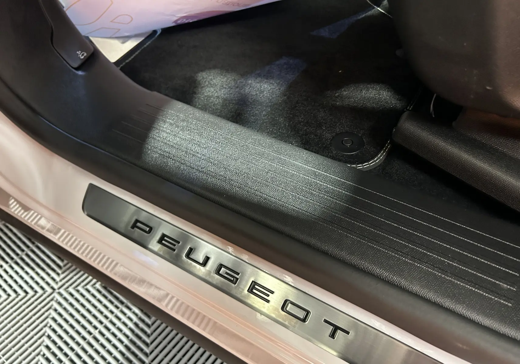 Gros plan sur la plaque de seuil de porte Peugeot et le tapis noir intérieur du Peugeot 3008 blanc Okenite.
