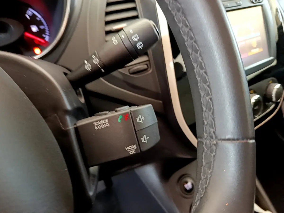 Gros plan sur la commande audio au volant cuir noir du Renault Captur Business gris foncé, avec tableau de bord et écran tactile en arrière-plan.