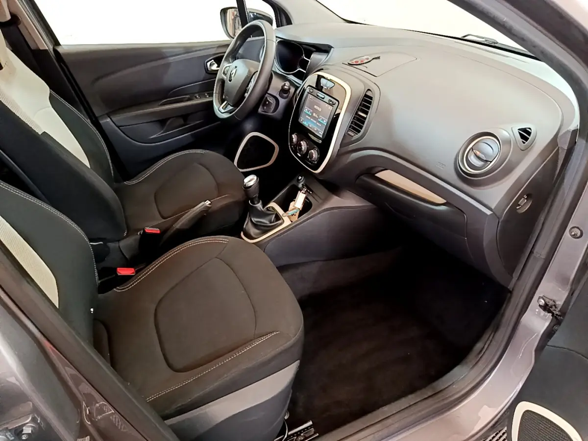 Vue intérieure côté conducteur du Renault Captur gris foncé, montrant tableau de bord avec écran tactile et volant cuir multifonctions.