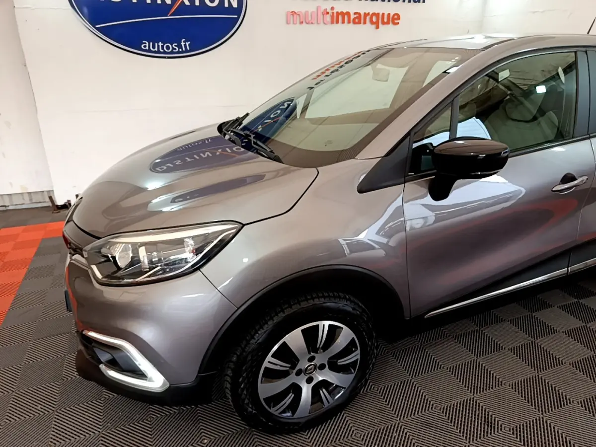 Vue 3/4 avant droit d'un Renault Captur gris foncé avec phares LED et jantes alliage visibles en intérieur showroom.