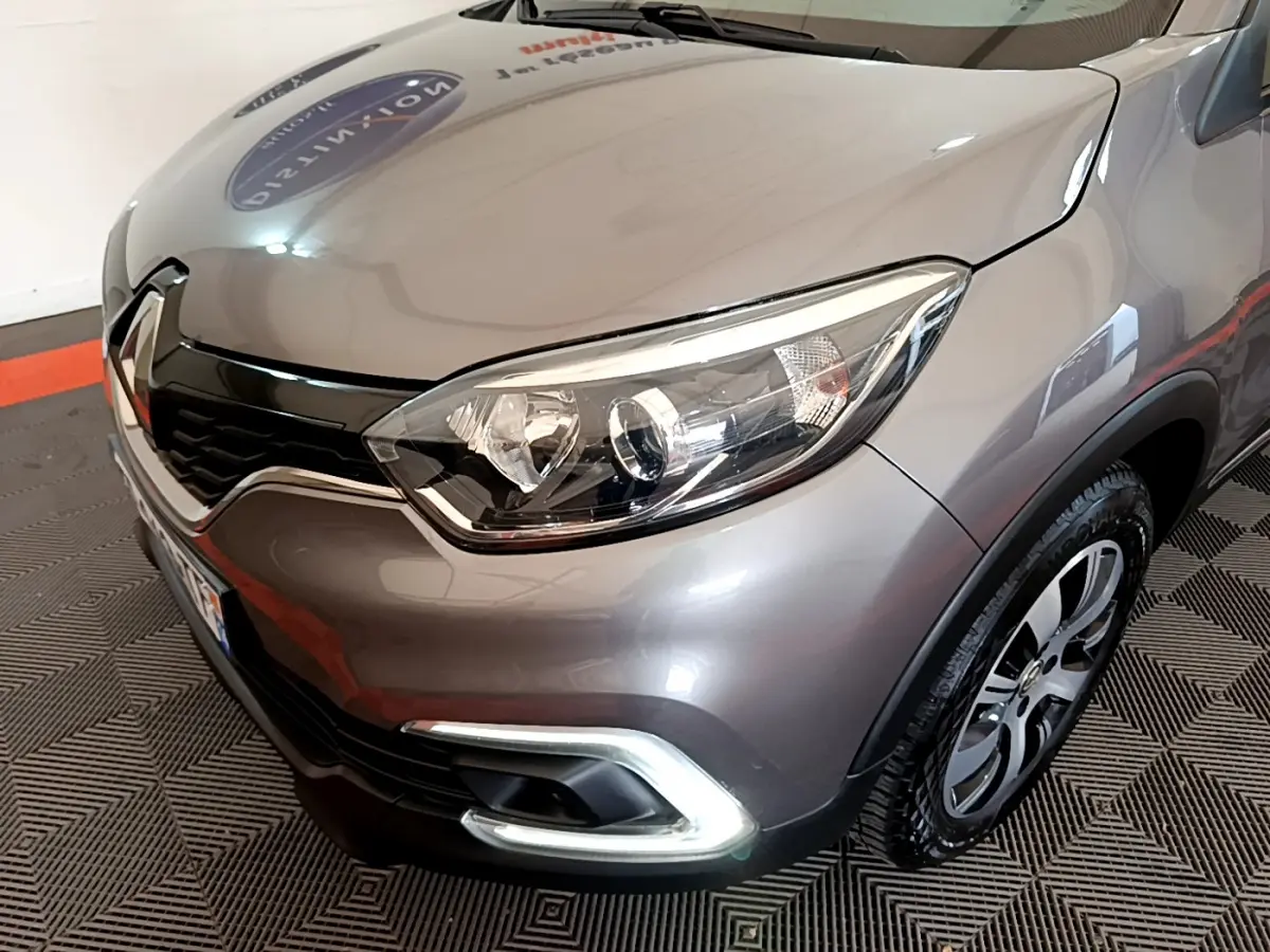 Vue 3/4 avant droit d'un Renault Captur gris foncé mettant en valeur son phare et sa calandre chromée.