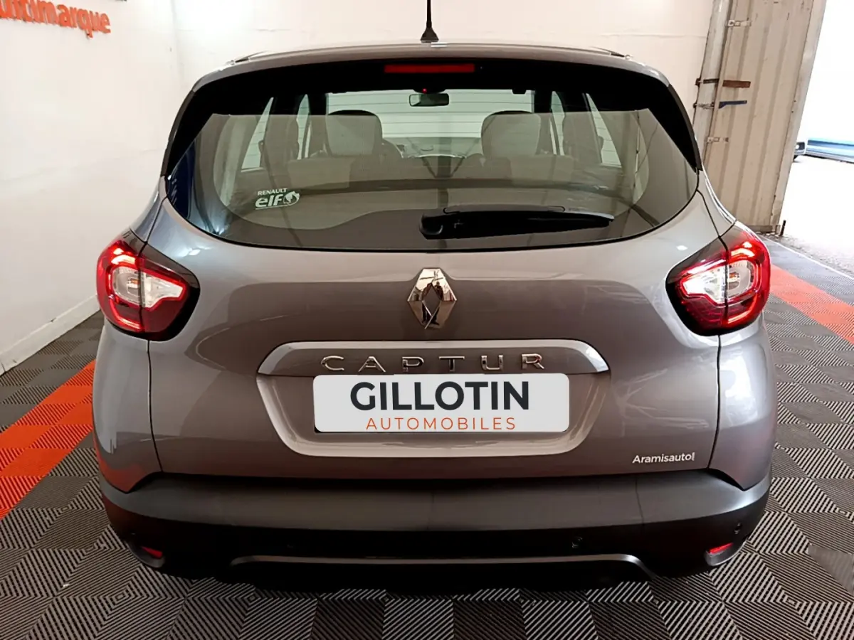 Vue arrière d'un Renault Captur gris foncé avec feux arrière allumés et logo centré sur le hayon.